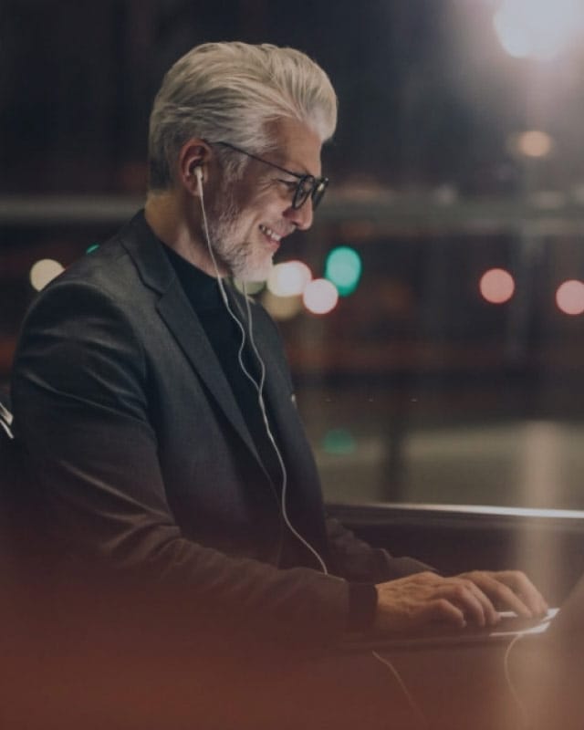POWR2_background_4 A man smiles with earphones in while looking at a laptop screen