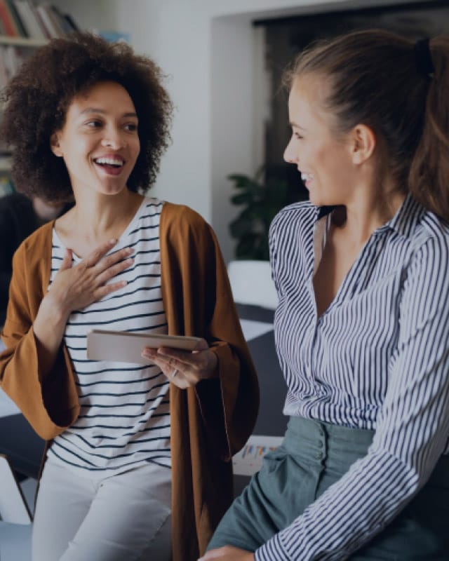 productside-tall Two women laugh at each other while one holds a notepad