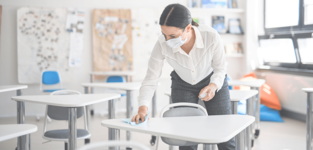picture-perfect-cleaning-background-1 Person wearing a face mask disinfecting desks in a classroom with a cleaning cloth and spray bottle