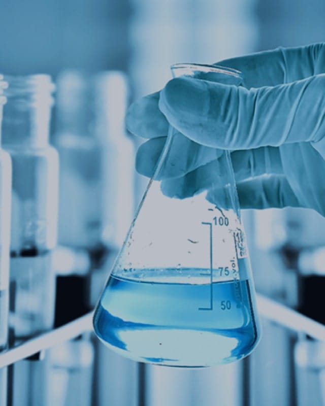 h2compliance-background-4 Background image for H2 Compiance's case study showing a gloved hand holding a laboratory flask with blue liquid